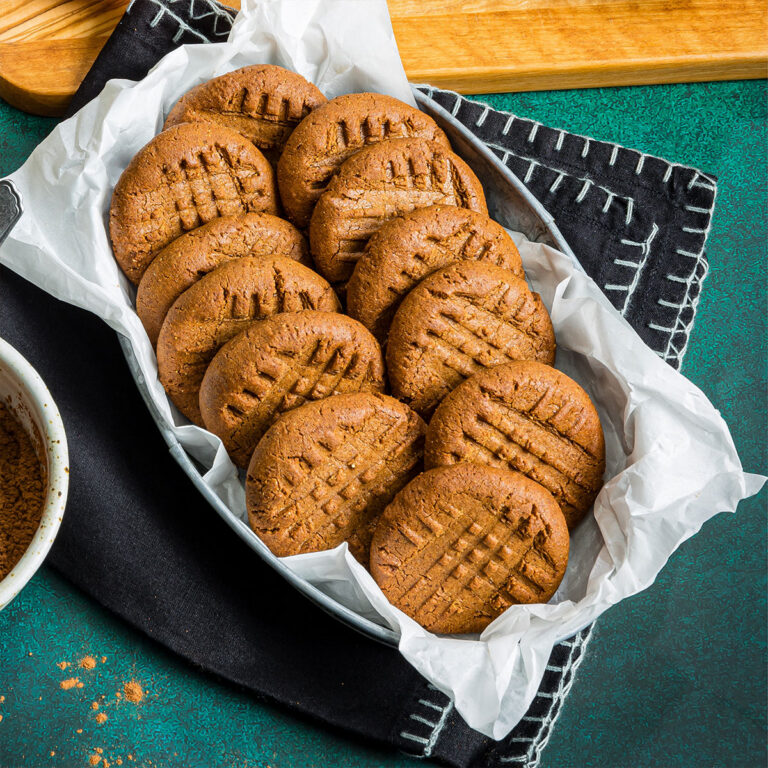 Pile of peanut butter cookies in a tin lined with parchment on a teal countertop.